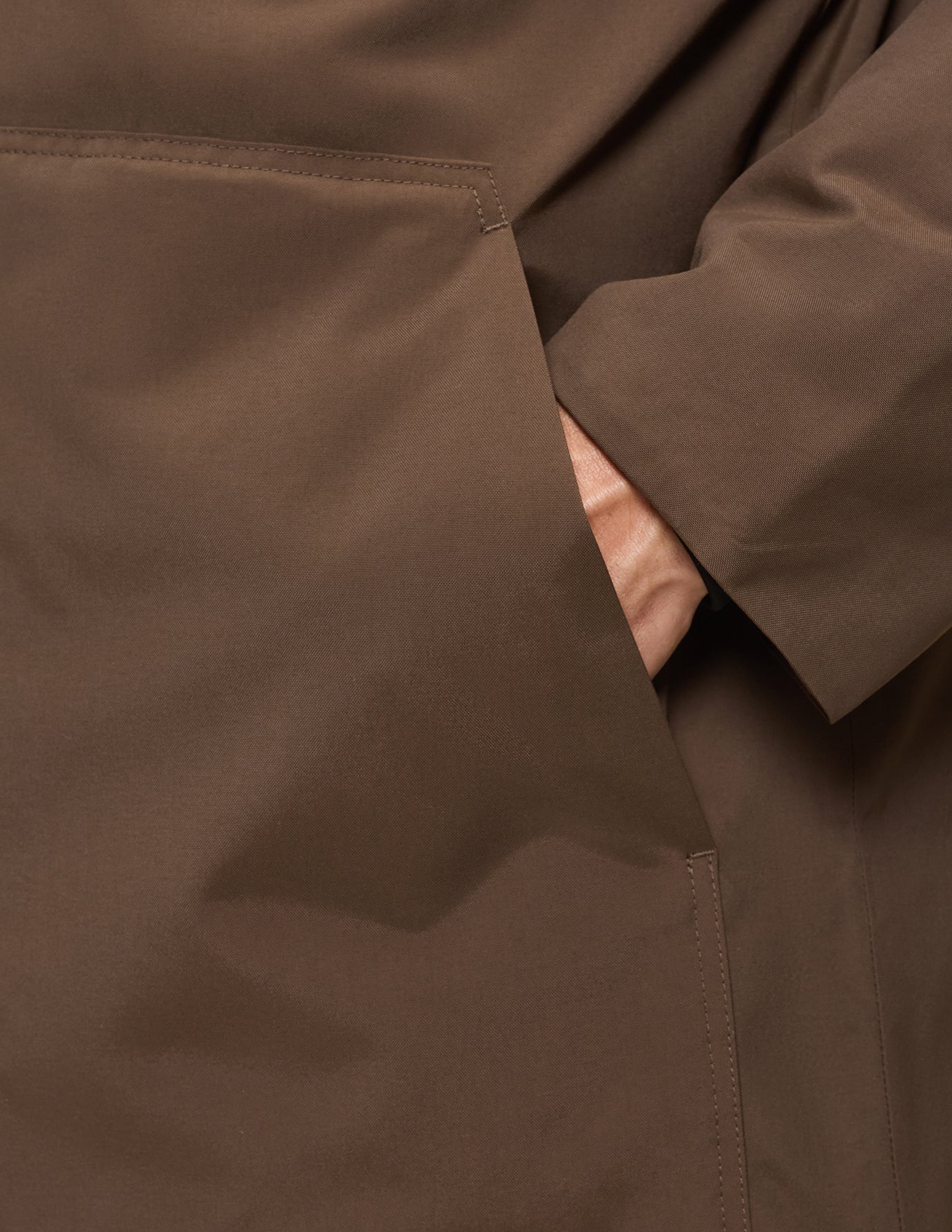 En hand instoppad i den stora sidfickan på en sadelbrun Utility Jacket.